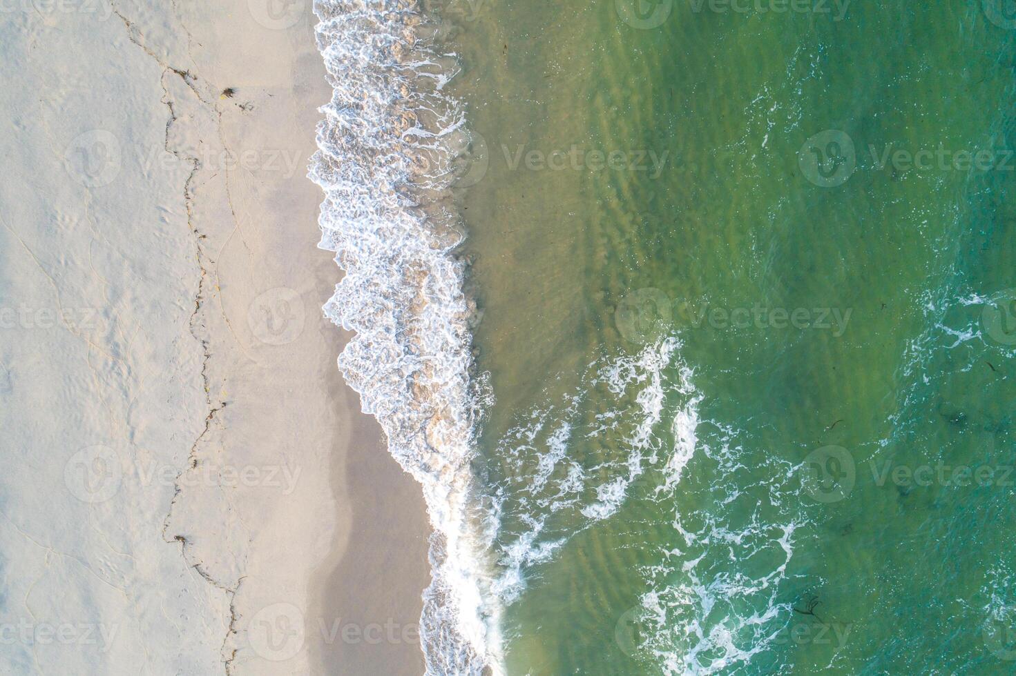 Beach sand sea shore with green wave and white foamy summer background. Overhead drone view photo