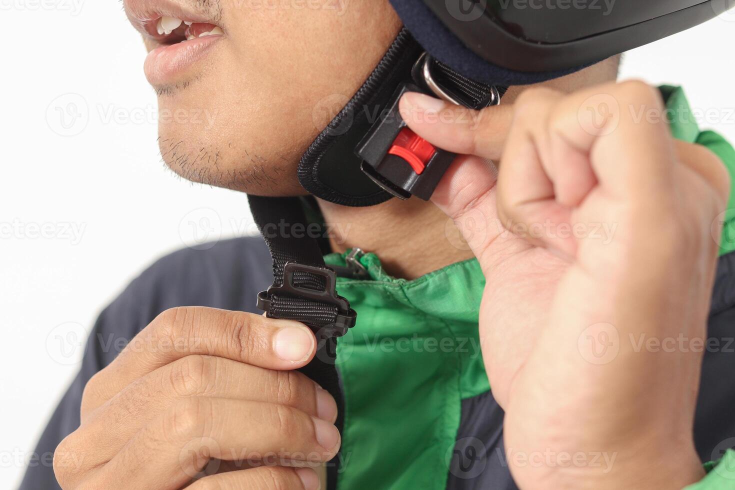 Close up portrait of Asian online taxi driver wearing green jacket and helmet demonstrating how to wear helmet correctly. Isolated image on white background photo