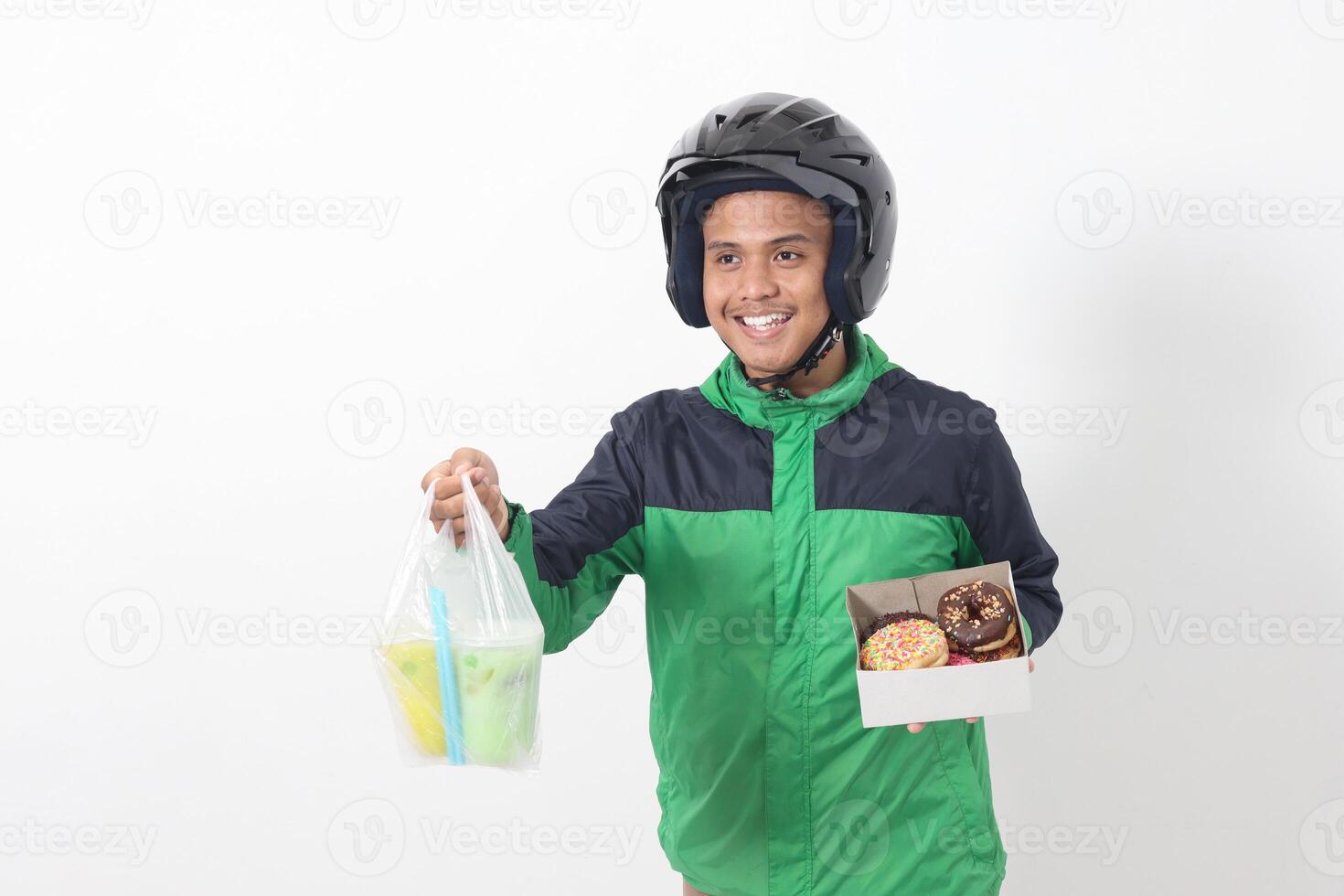 Portrait of Asian online taxi driver wearing green jacket and helmet holding a box of donuts and cup of juice drink, delivering to customer. Isolated image on white background photo