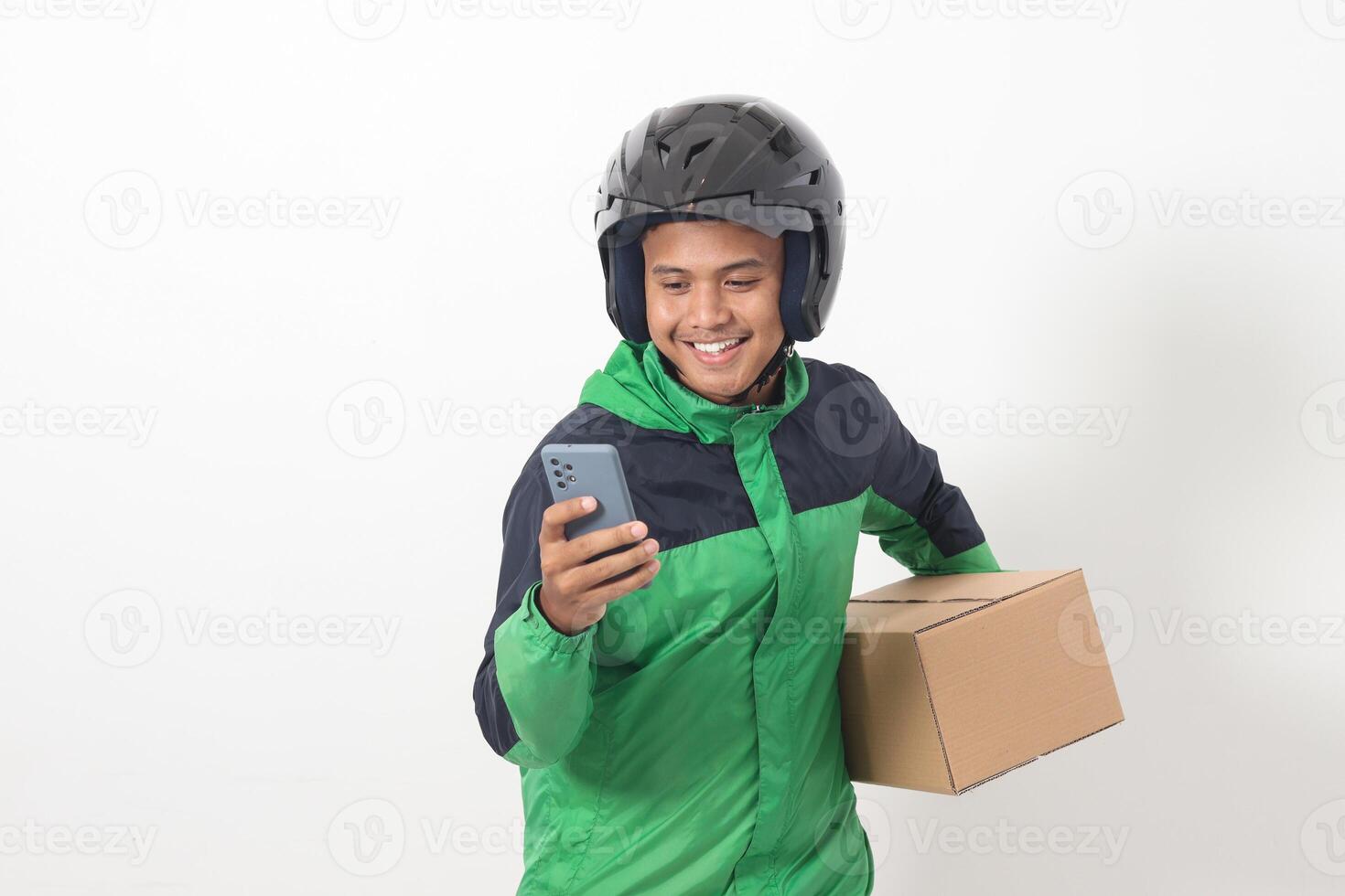 Portrait of Asian online courier driver wearing green jacket and helmet delivering package and box for customer while using mobile phone and taking order. Isolated image on white background photo