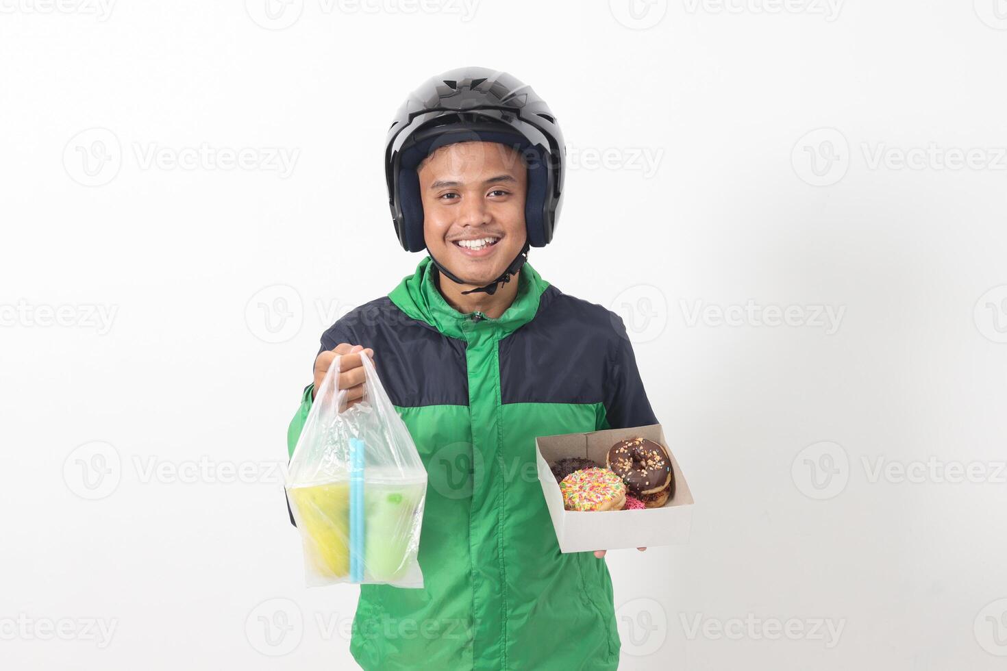 Portrait of Asian online taxi driver wearing green jacket and helmet holding a box of donuts and cup of juice drink, delivering to customer. Isolated image on white background photo