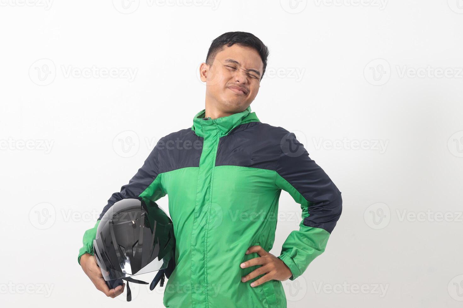 Portrait of tired Asian online taxi driver wearing green jacket holding a helmet on hip and feeling exhausted. Isolated image on white background photo