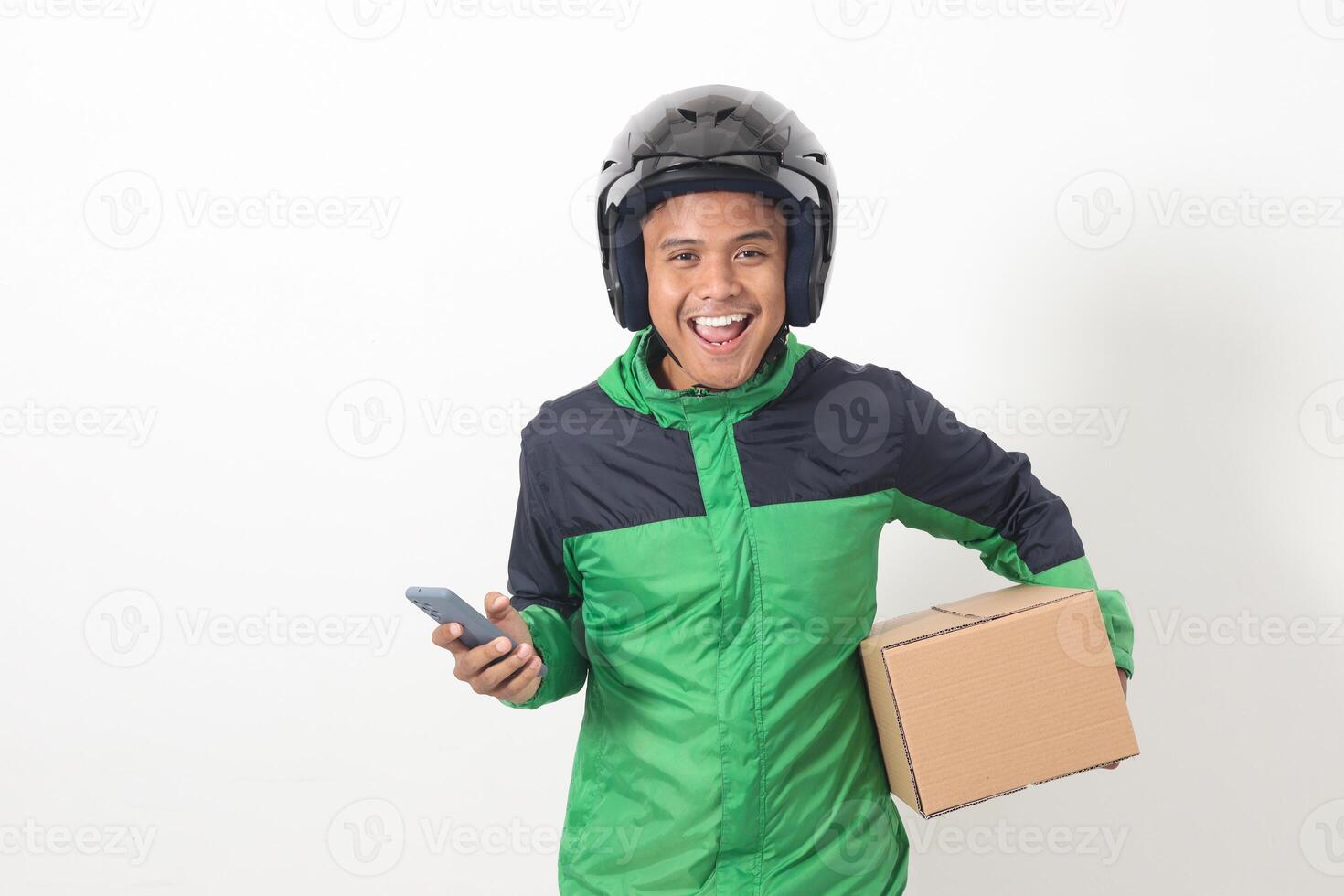 Portrait of Asian online courier driver wearing green jacket and helmet delivering package and box for customer while using mobile phone and taking order. Isolated image on white background photo