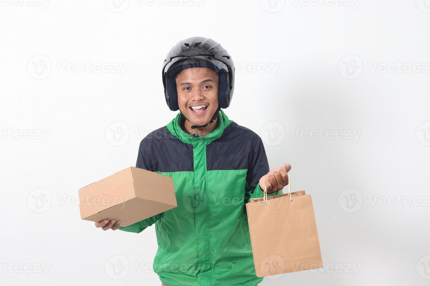 Portrait of Asian online courier driver wearing green jacket and helmet giving craft paper shopping bag and box package. Isolated image on white background photo