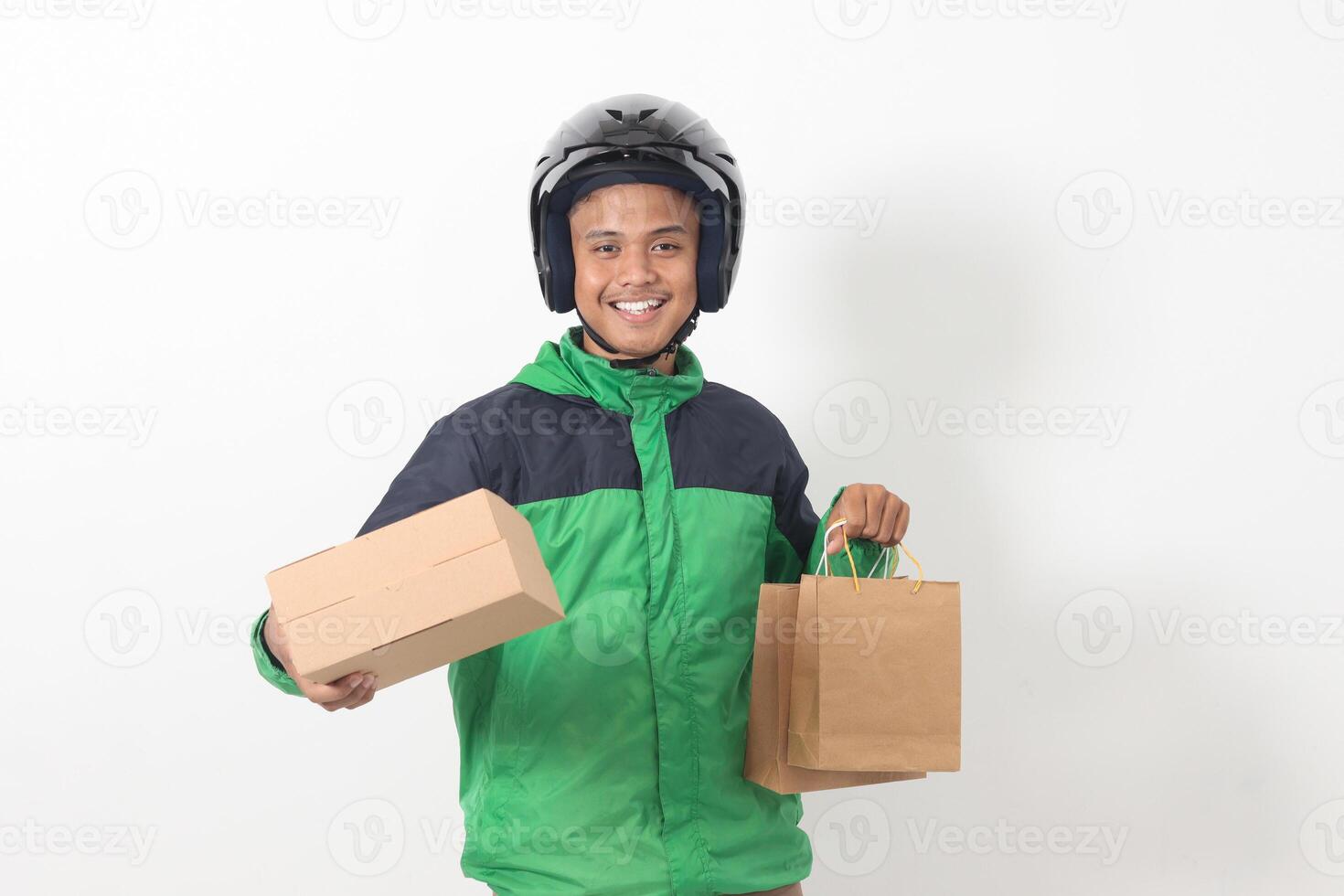 Portrait of Asian online courier driver wearing green jacket and helmet giving craft paper shopping bag and box package. Isolated image on white background photo