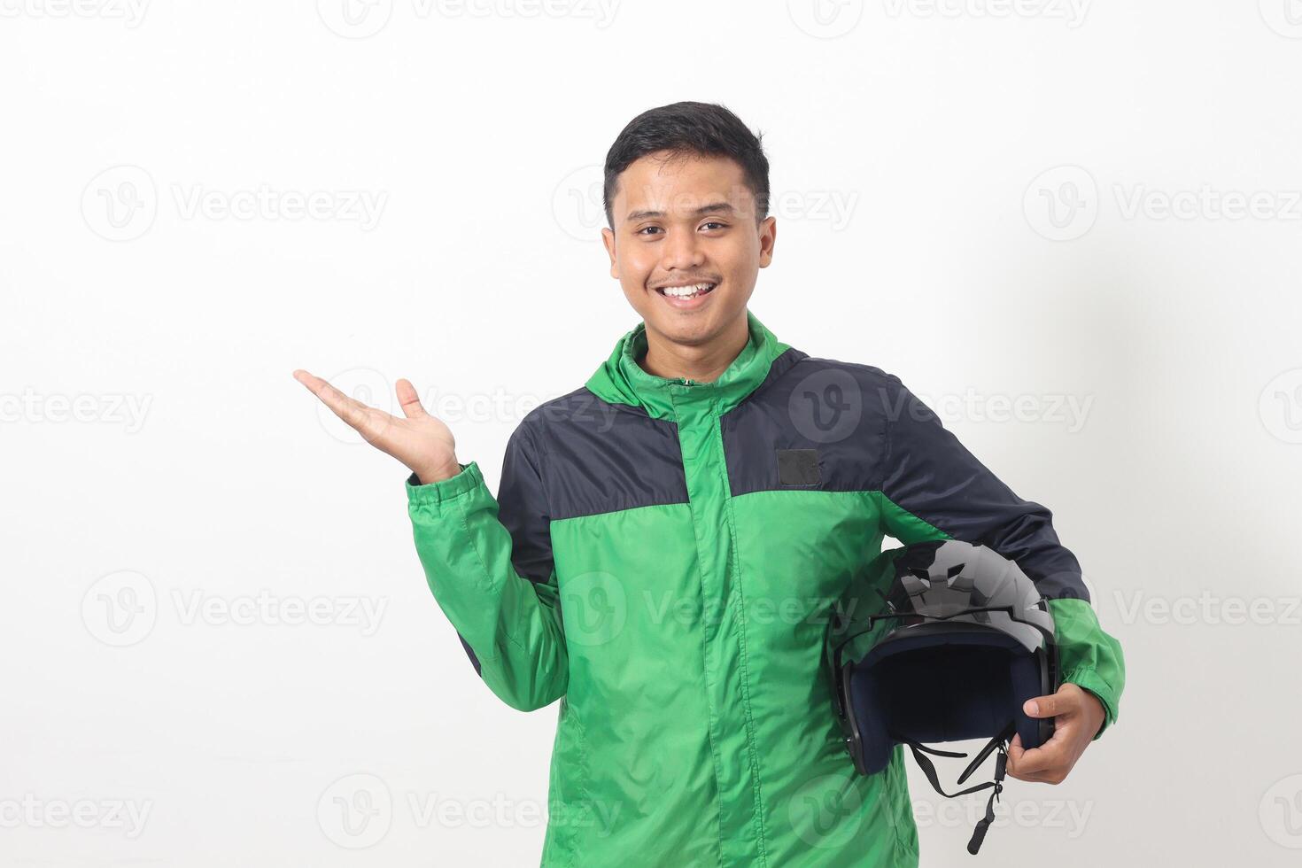 Portrait of Asian online taxi driver wearing green standing against white background, smiling and looking at camera, holding his helmet on the side photo