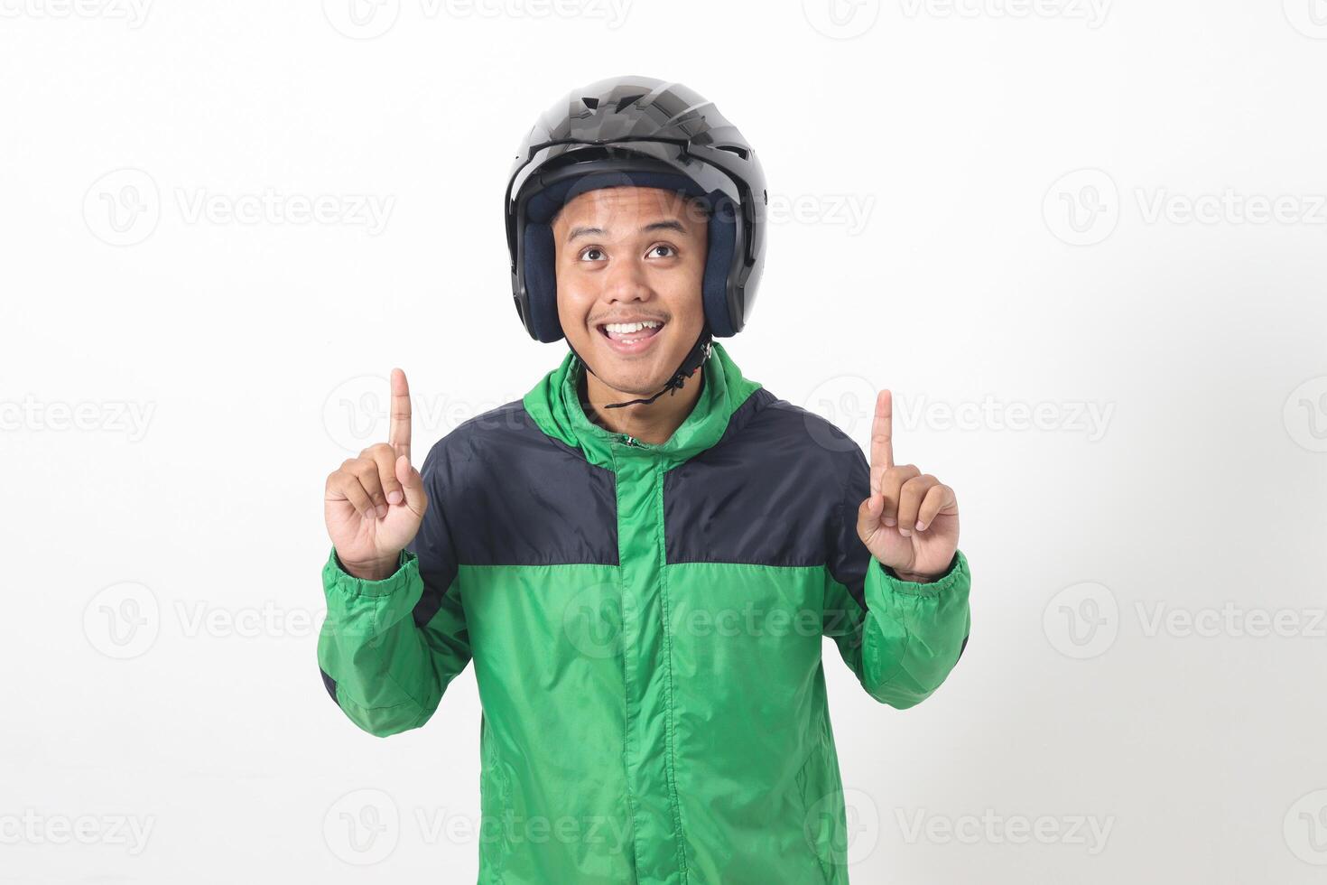 Portrait of Asian online taxi driver wearing green jacket and helmet pointing at empty space with finger. Isolated image on white background photo