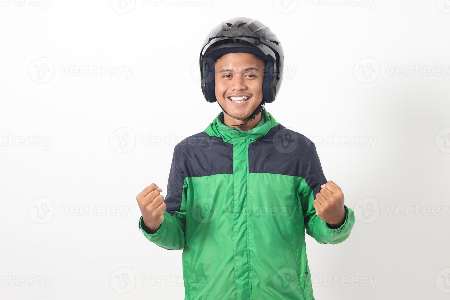Portrait of Asian online taxi driver wearing green jacket and helmet raising his fist, celebrating success. Isolated image on white background photo