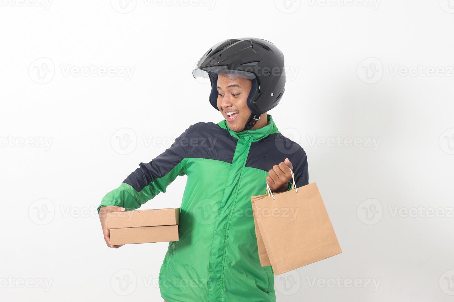 Portrait of Asian online courier driver wearing green jacket and helmet giving craft paper shopping bag and box package. Isolated image on white background photo