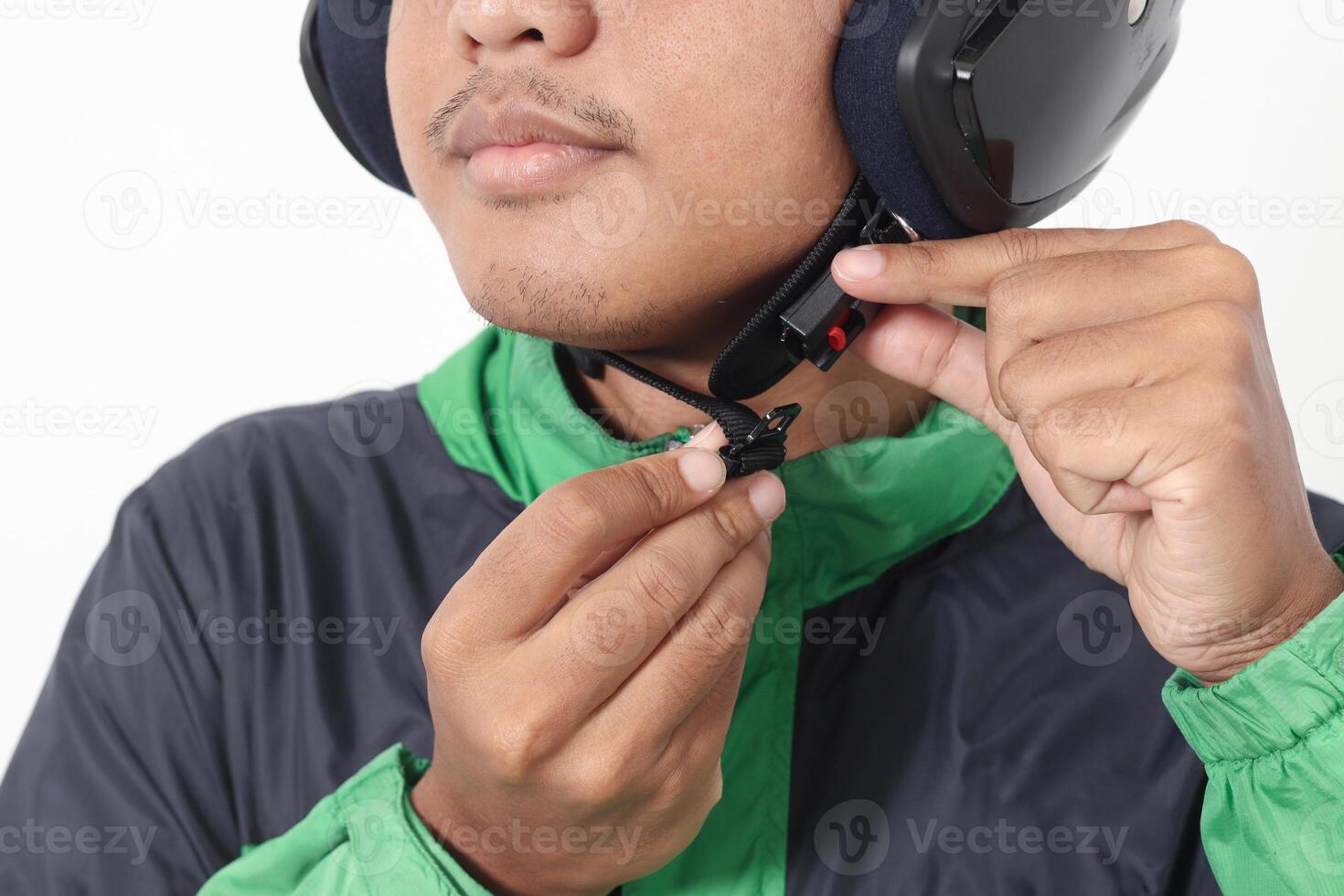 Close up portrait of Asian online taxi driver wearing green jacket and helmet demonstrating how to wear helmet correctly. Isolated image on white background photo