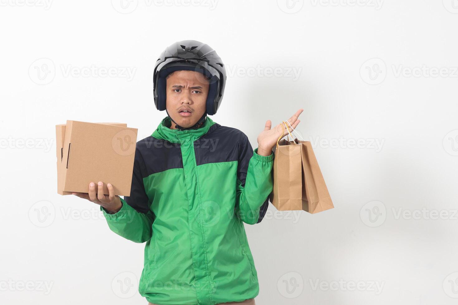 Portrait of Asian online courier driver wearing green jacket and helmet giving craft paper shopping bag and box package. Isolated image on white background photo