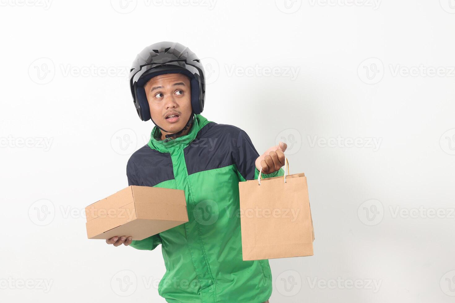Portrait of Asian online courier driver wearing green jacket and helmet giving craft paper shopping bag and box package. Isolated image on white background photo