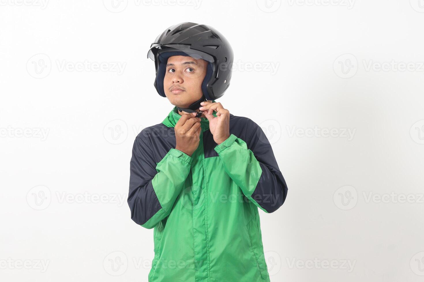 Portrait of Asian online taxi driver wearing green jacket and helmet demonstrating how to wear helmet correctly. Isolated image on white background photo
