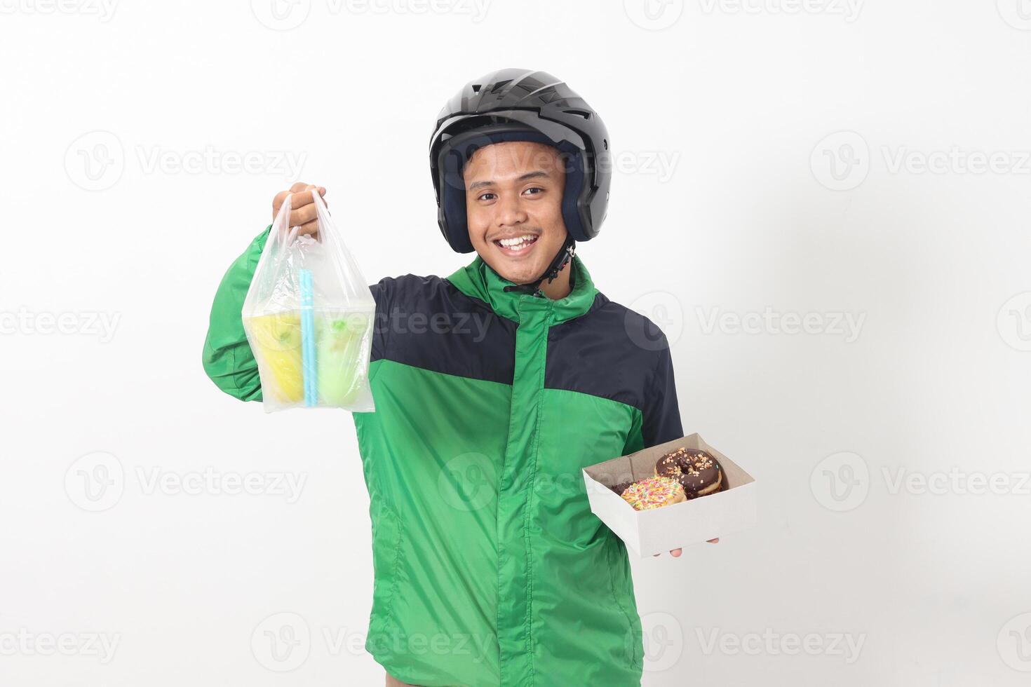 Portrait of Asian online taxi driver wearing green jacket and helmet holding a box of donuts and cup of juice drink, delivering to customer. Isolated image on white background photo