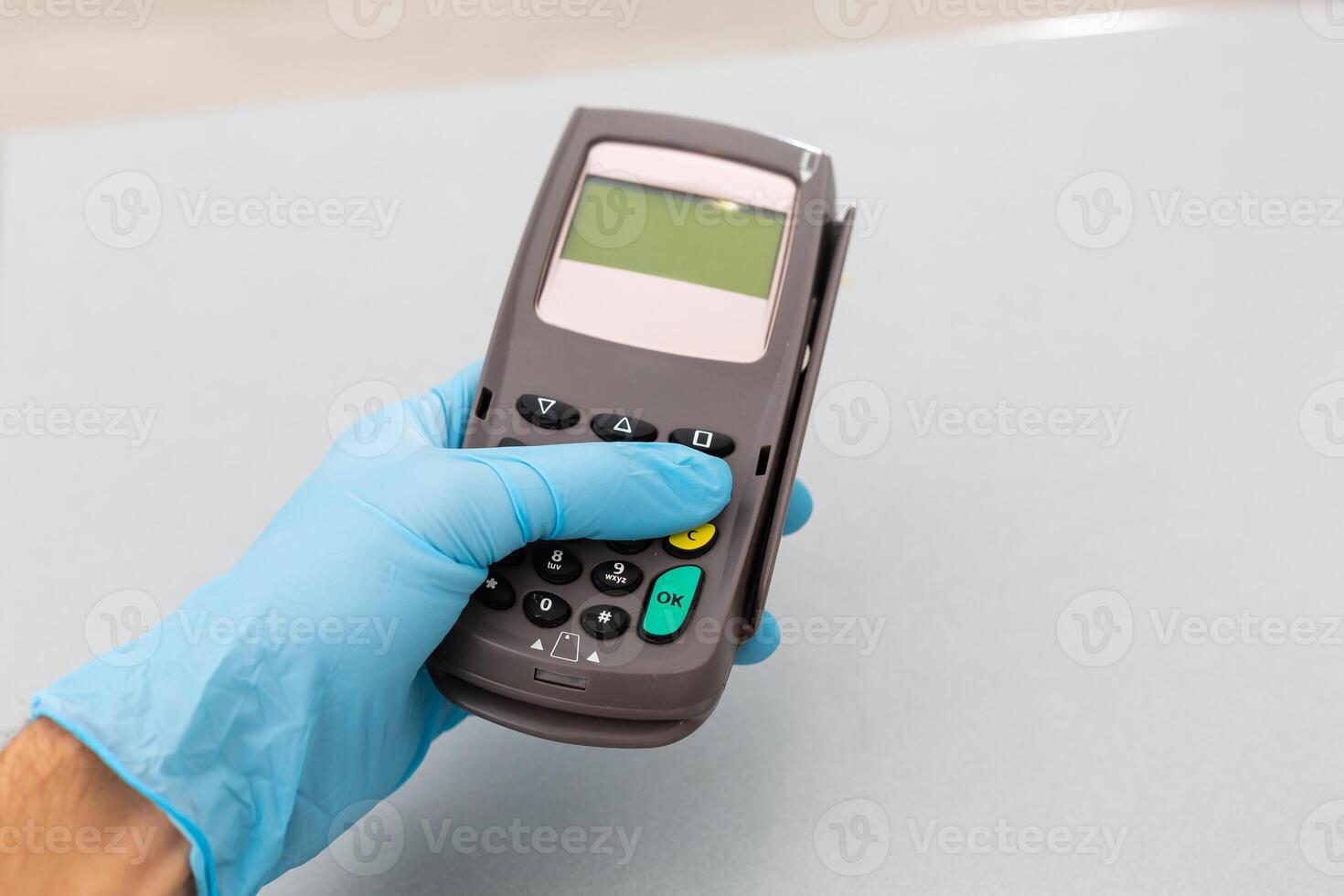 Cashier hand holding credit card reader machine and wearing disposable gloves, paying with smartphone during Covid-19 pandemic. photo