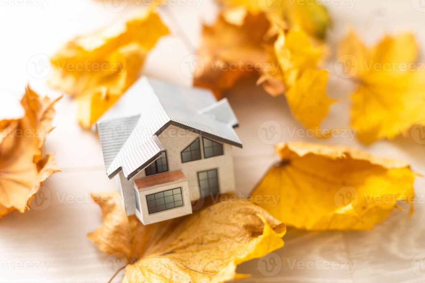 Autumnal Background. Toy house and dried orange fall maple leaves on grey knitted sweater. Thanksgiving banner copy space. Hygge mood cold weather concept. Hello Autumn with family. photo