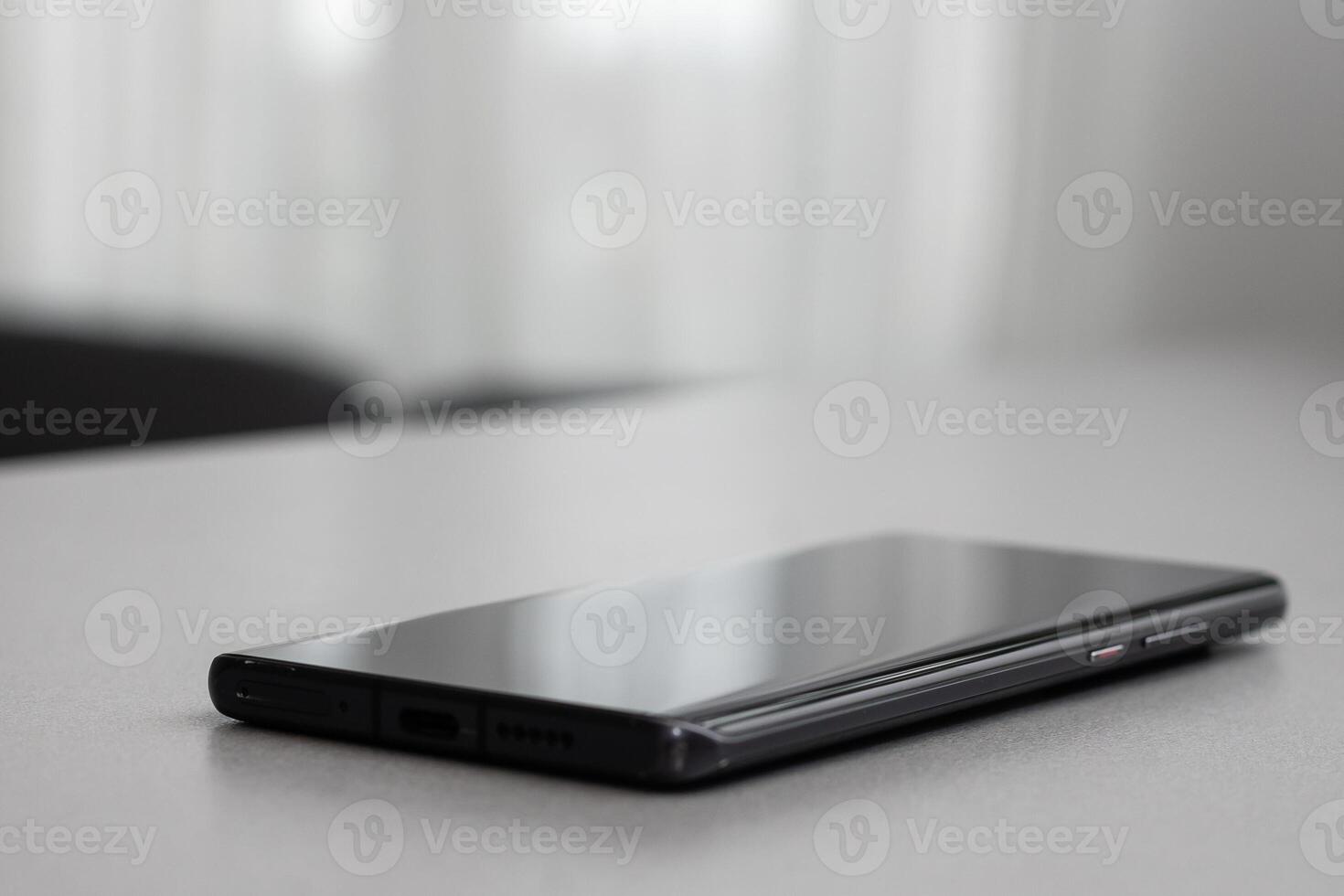 Black modern mobile phone with blank screen on black stone table background. Smartphone on old dark grey vintage texture background. photo