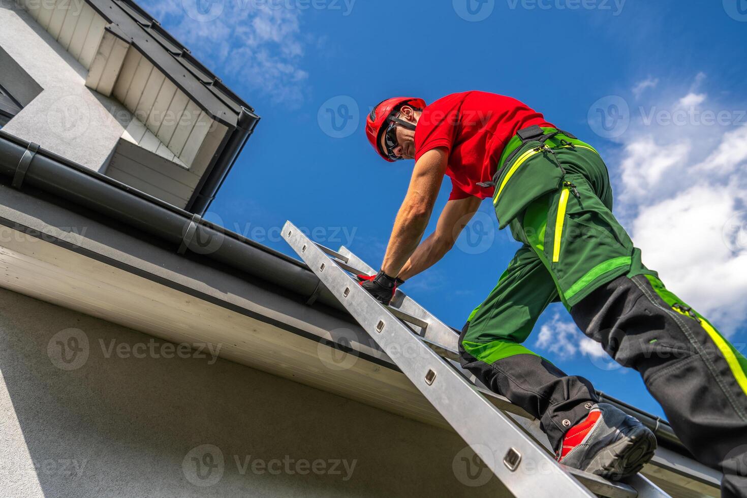 Professional Maintenance Worker Climbing a Ladder to Repair Roof Gutter on a Sunny Day photo