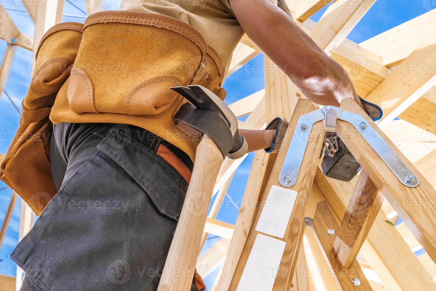 Construction Worker Using a Wooden Ladder to Build a Structure Under a Clear Blue Sky photo