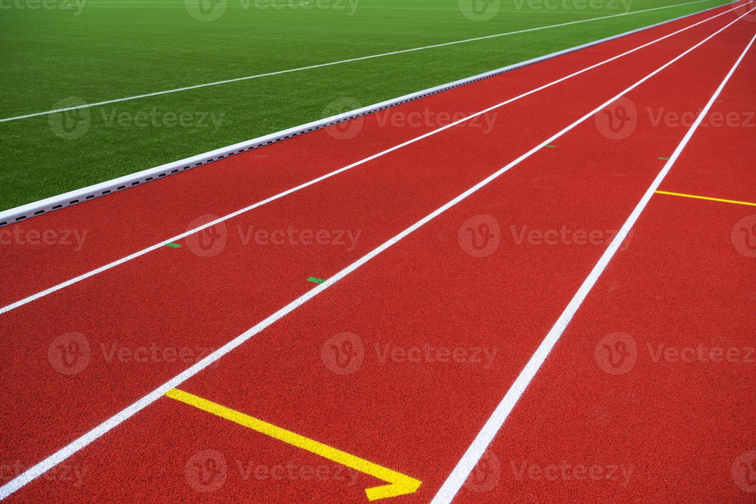 A Vibrant Red Running Track With Bright Yellow Lane Markings Near a Green Field on a Sunny Day photo