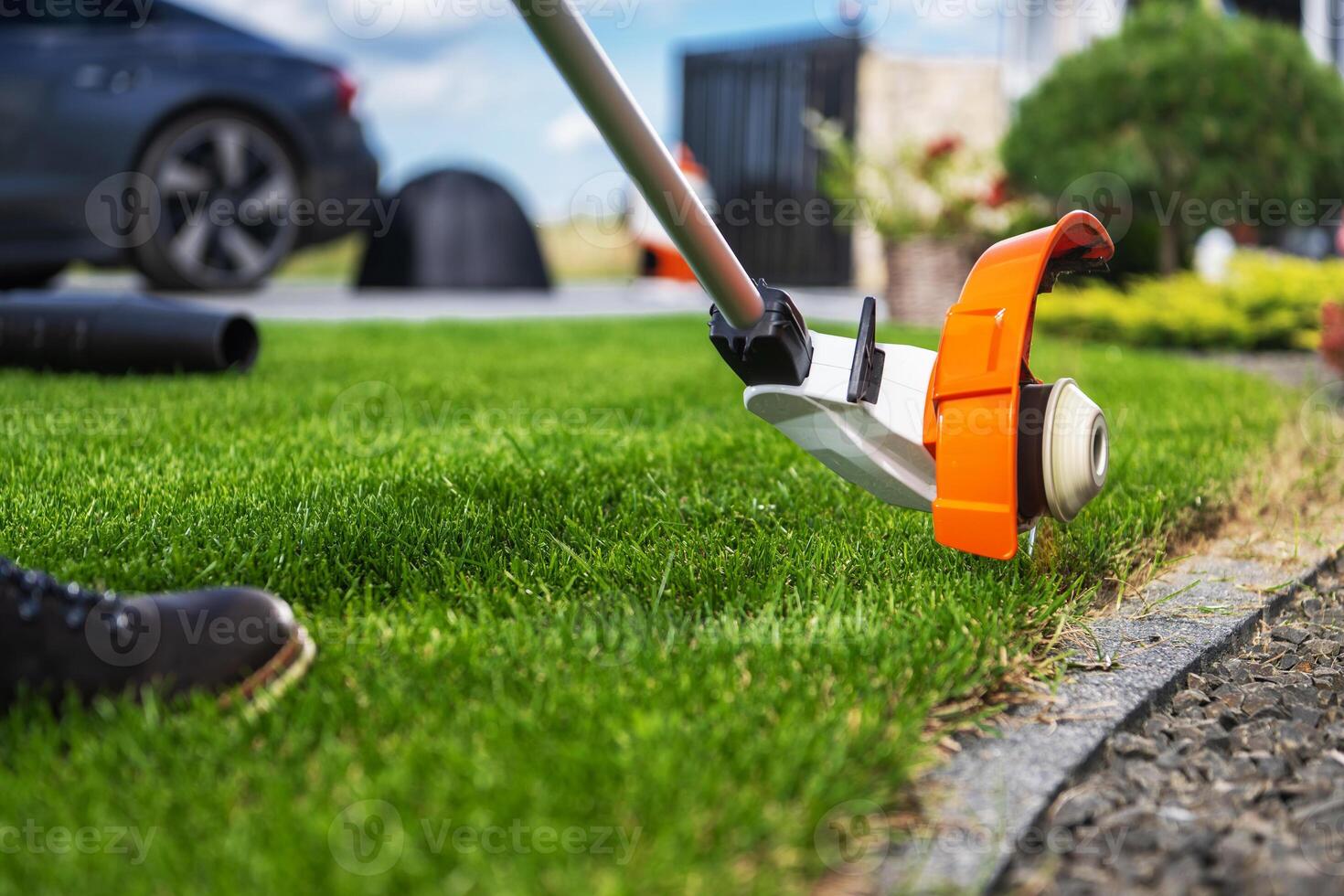 Trimming Lush Green Grass Along a Driveway With a Weed Eater on a Sunny Day in a Suburban Garden photo