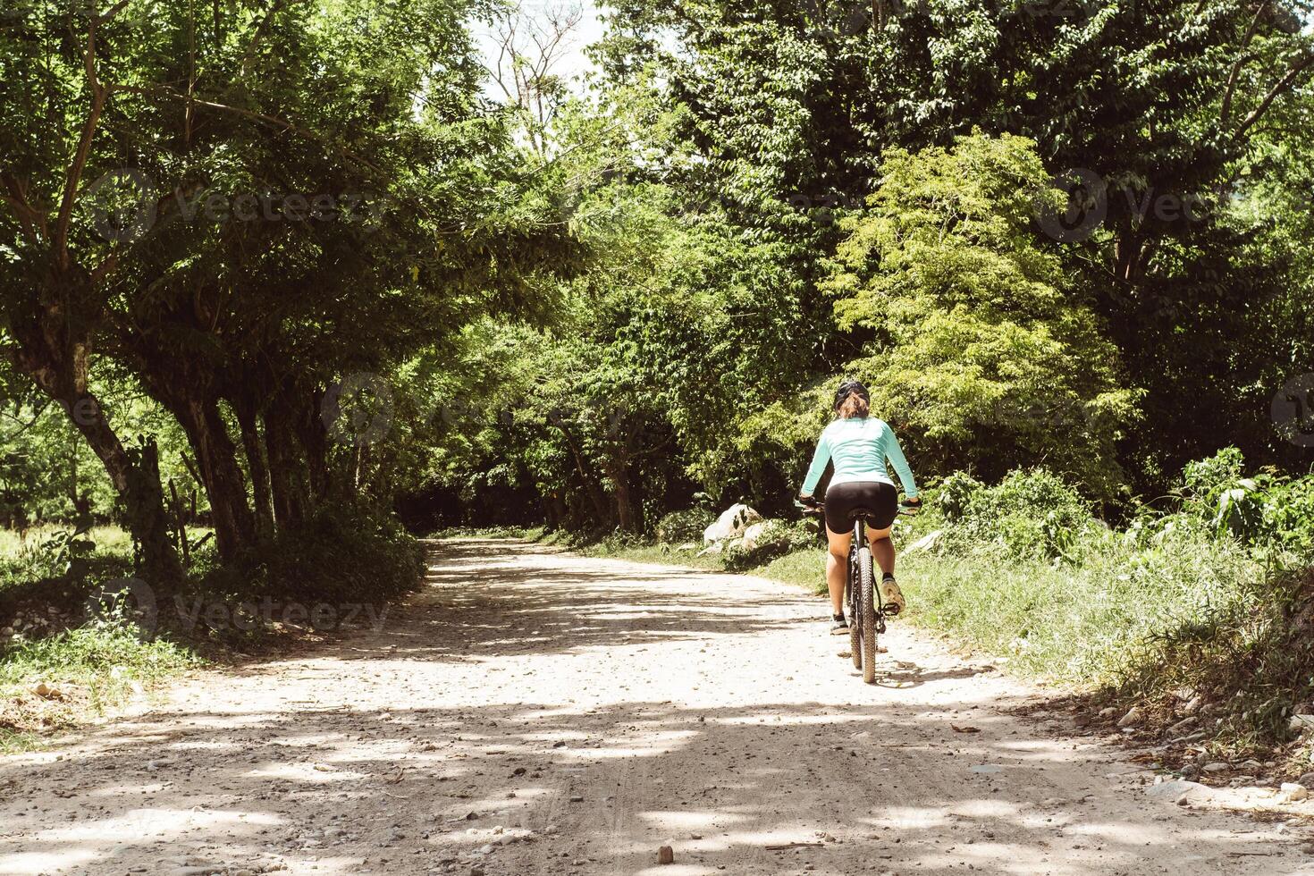 horizontal shot from behind of a female cyclist riding a bicycle running on a dirt road. mountain bike concept. photo