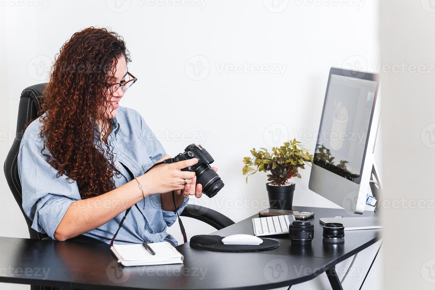 Latin American woman checking a photo camera at a desk.