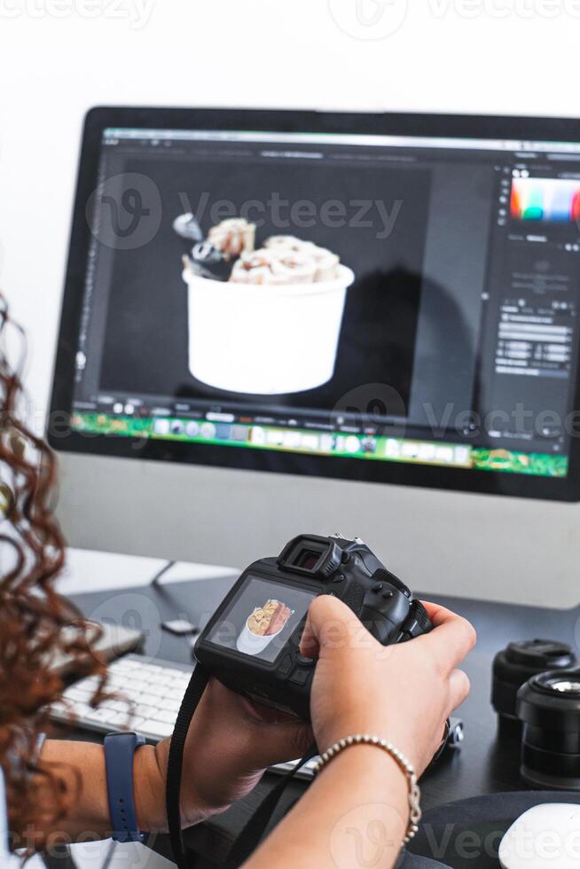 Hands of a person holding a camera while working on a computer editing photos. photo