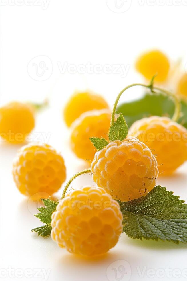 A group of yellow raspberries with leaves on a white surface photo