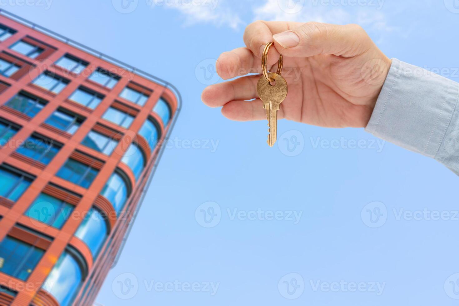 Apartment key in a man's hand. Brass house door lock key. Modern building, view from below. Architecture in modern city. Sale and rental of real estate. photo