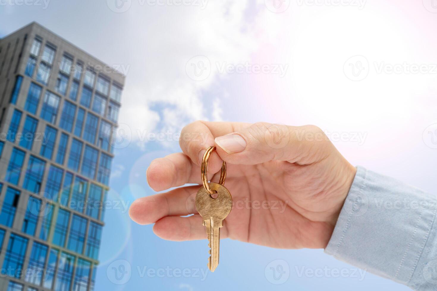 Apartment key in a man's hand. Brass house door lock key. High-rise buildings of modern city. View from below. photo