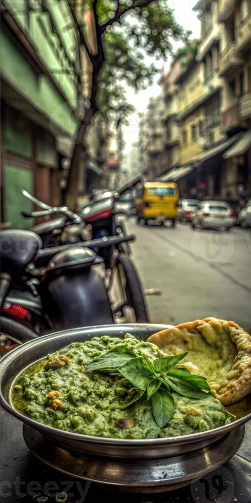A bowl of food with green herbs sits on a table in front of a motorcycle. The scene is set in a city street with cars and a truck in the background photo