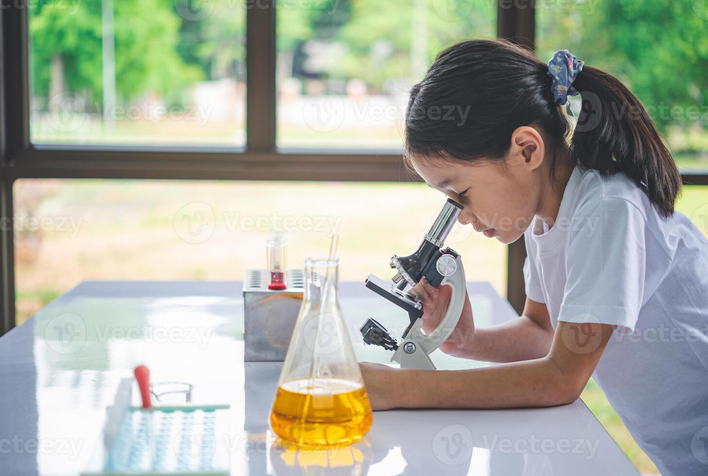 little scientist looking through a microscope and test tubes filled with chemicals for learning about science and experiments. photo