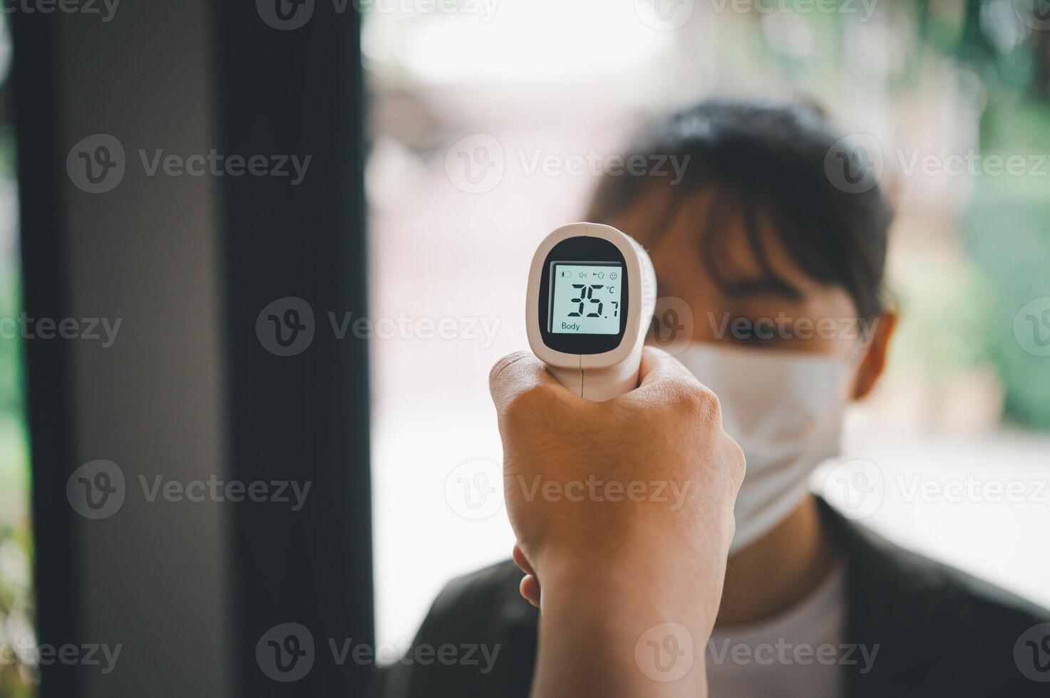 Hand holding infrared thermometer to measuring temperature people with face mask on background. Covid flu screening 19 concept. photo