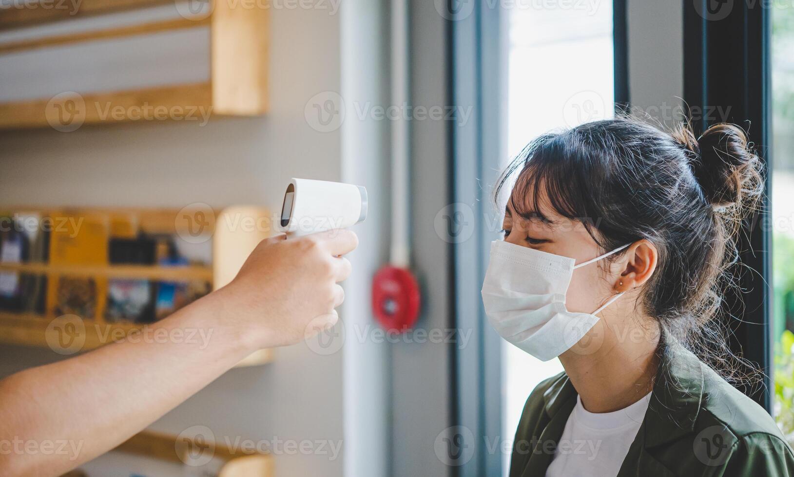 Hand holding infrared thermometer to measuring temperature people with face mask on background. Covid flu screening 19 concept. photo
