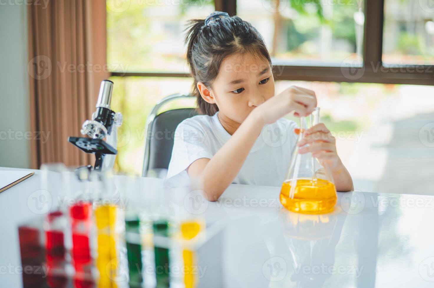 little scientist looking through a microscope and test tubes filled with chemicals for learning about science and experiments. photo