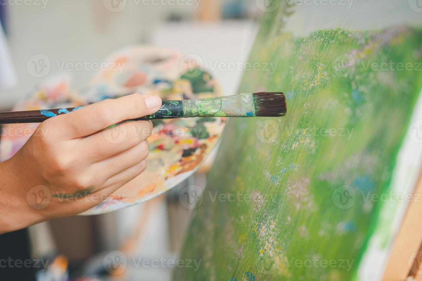close-up art student's hand using watercolor paint brush painting on canvas doing some art projects on studio workshop photo