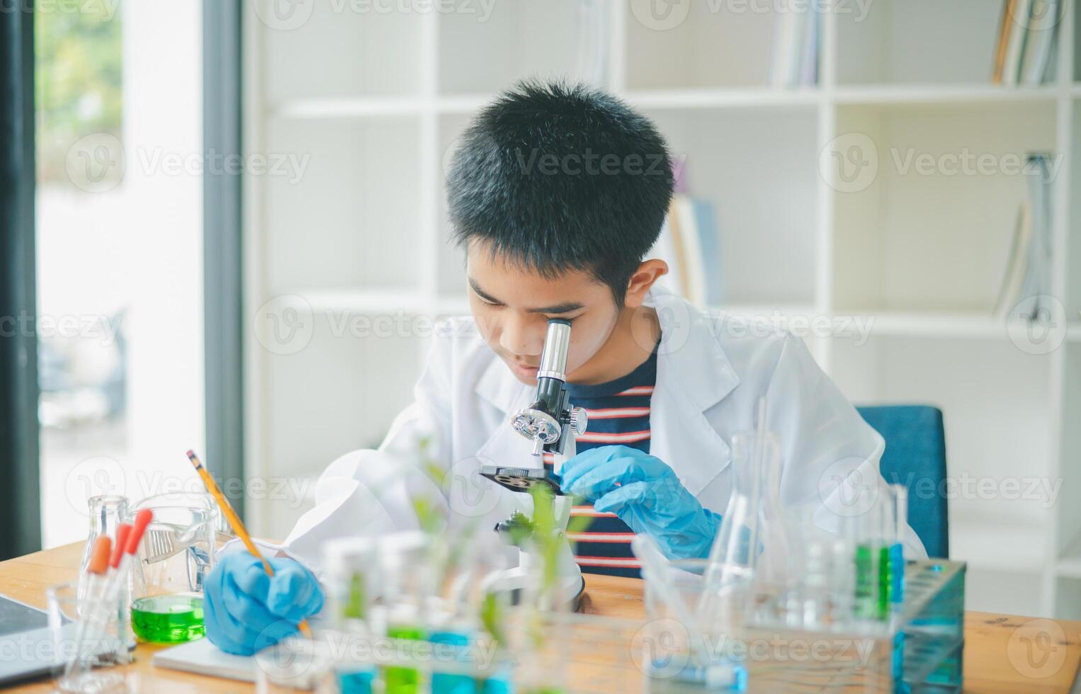 Asian male science students looking through a microscope and tests of plants in the classroom. Learning about scientific experiments on plant species. photo