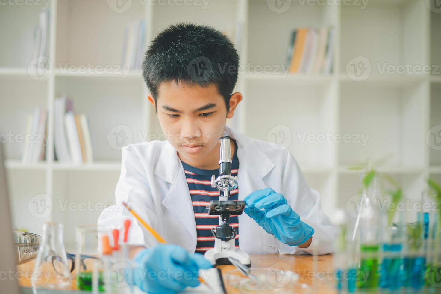 Asian male science students looking through a microscope and tests of plants in the classroom. Learning about scientific experiments on plant species. photo