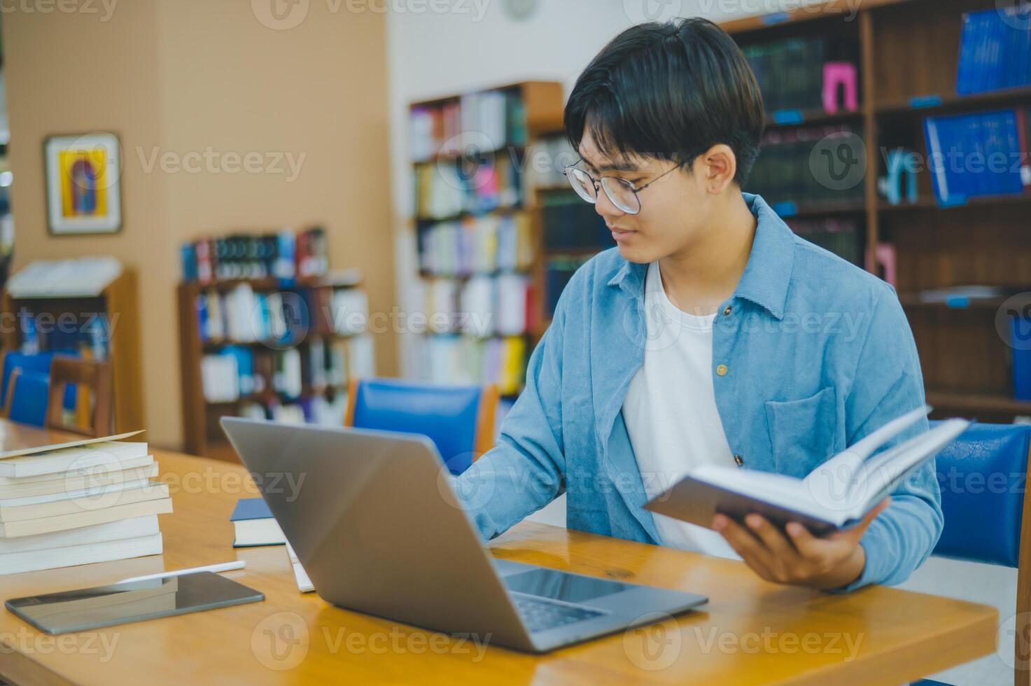 Male college students are working on laptops and searching for books to study, make reports, find useful information in college room. Concept of reading, learning and intelligence. photo