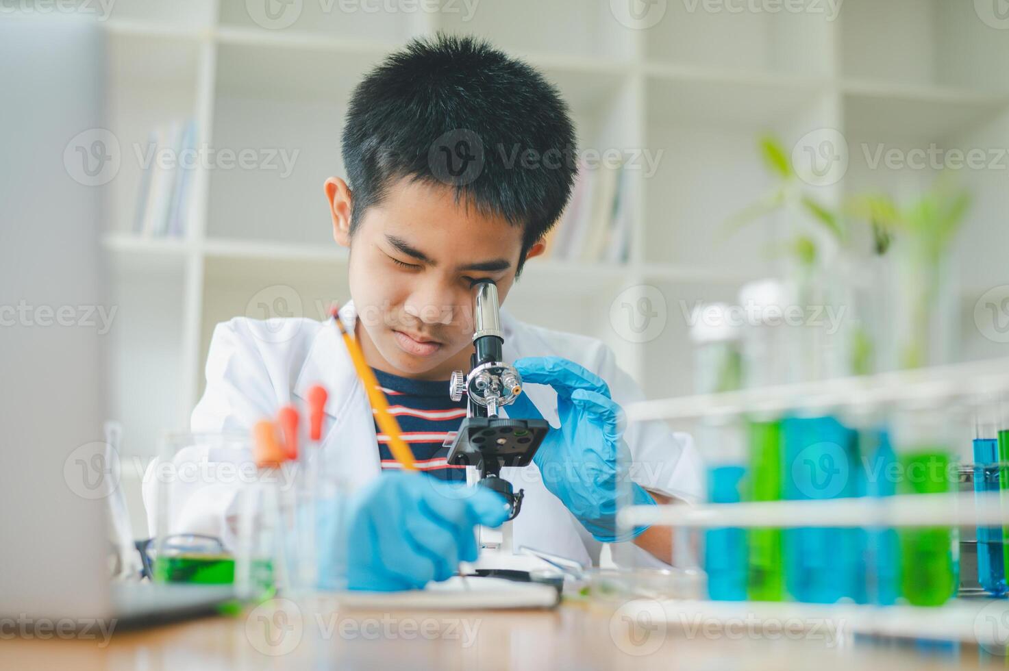 Asian male science students looking through a microscope and tests of plants in the classroom. Learning about scientific experiments on plant species. photo