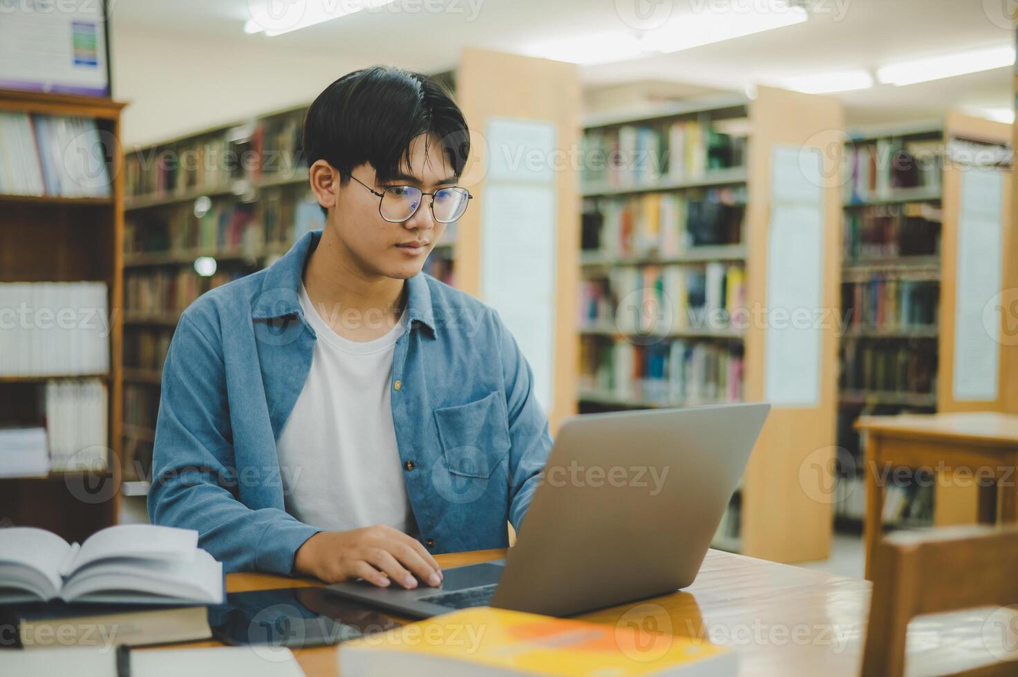 Male college students are working on laptops and searching for books to study, make reports, find useful information in college room. Concept of reading, learning and intelligence. photo