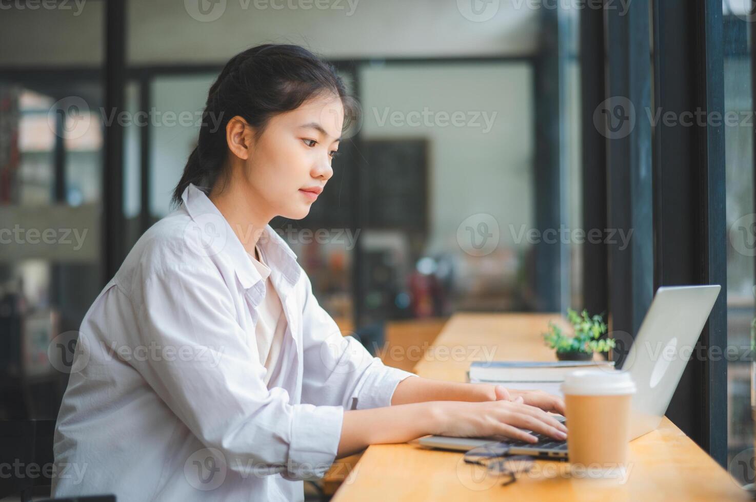 Young Asian college student working and learning on laptop In the cafe. Searching for knowledge online. photo
