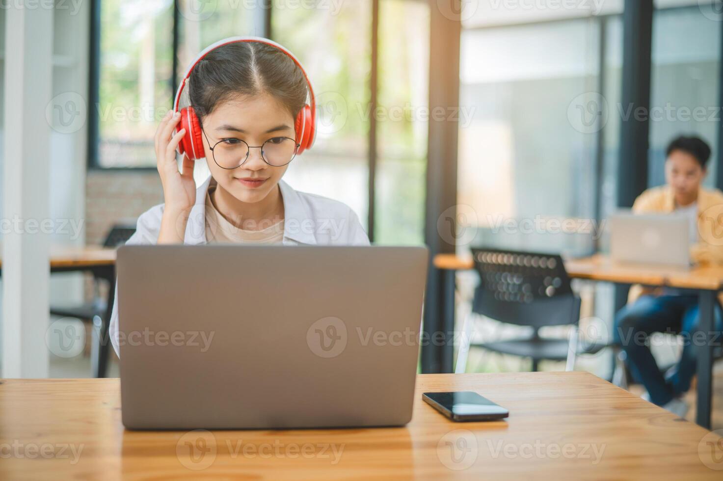 Student using a laptop in a cafe while wearing headphones, learning and searching the internet, and making a call. photo