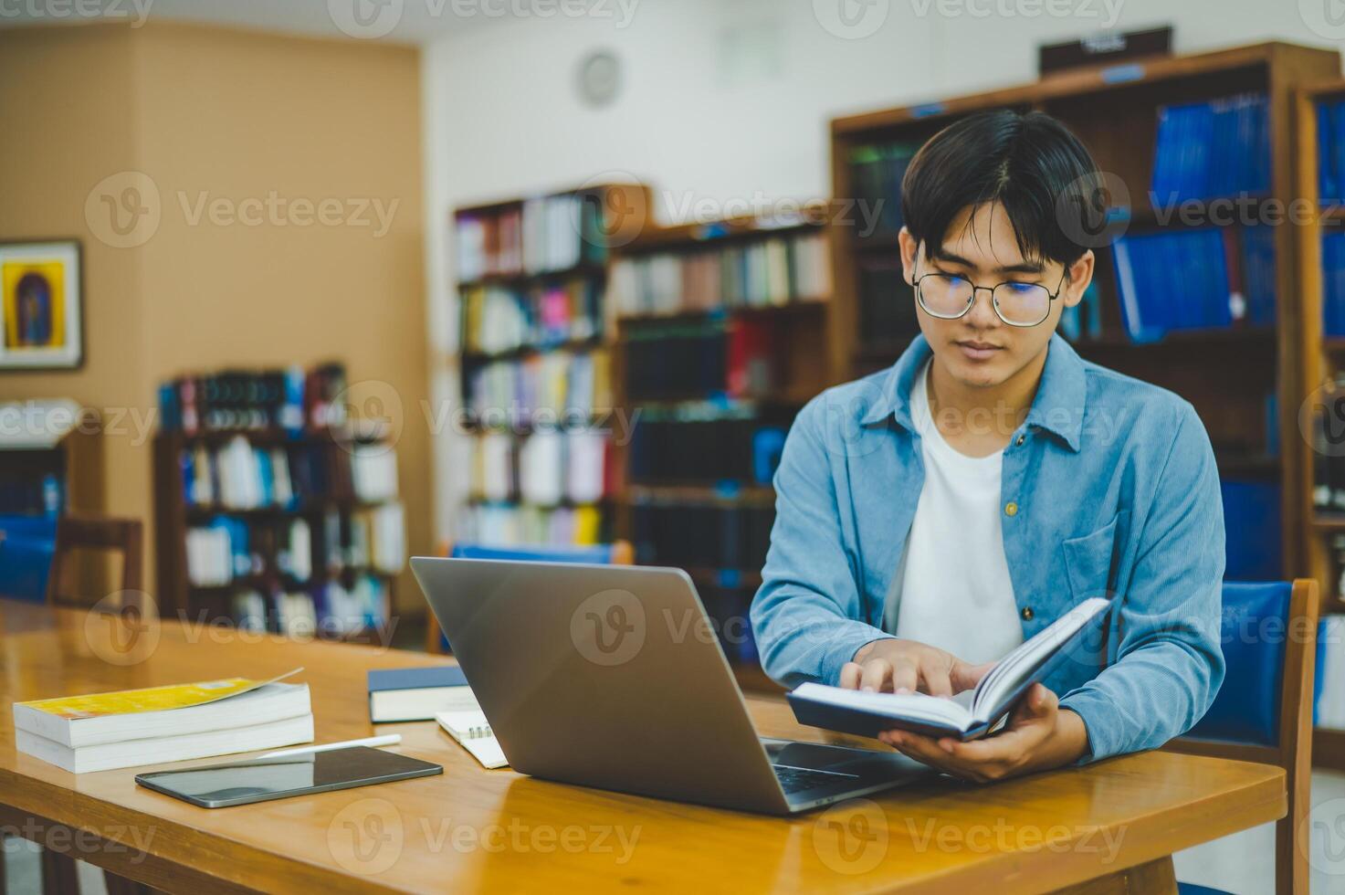 Male college students are working on laptops and searching for books to study, make reports, find useful information in college room. Concept of reading, learning and intelligence. photo