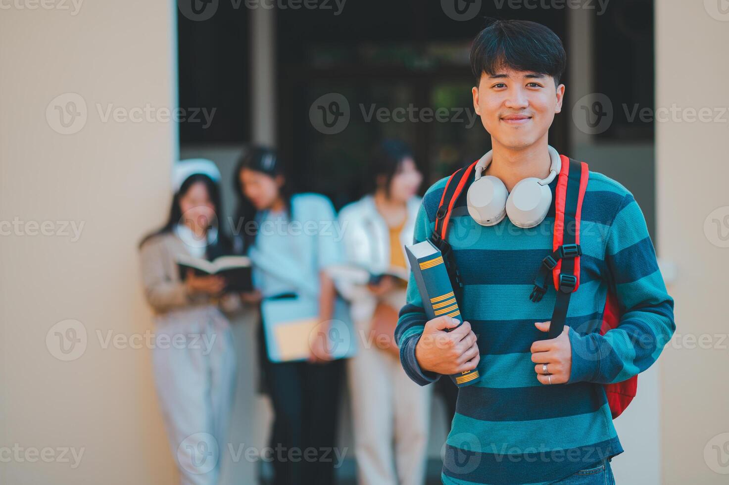 A young man is smiling and holding a book and a backpack photo