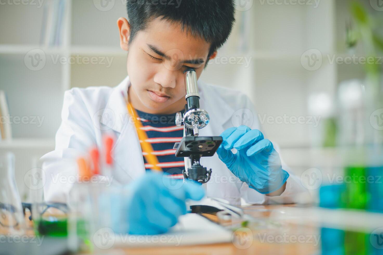 Asian male science students looking through a microscope and tests of plants in the classroom. Learning about scientific experiments on plant species. photo
