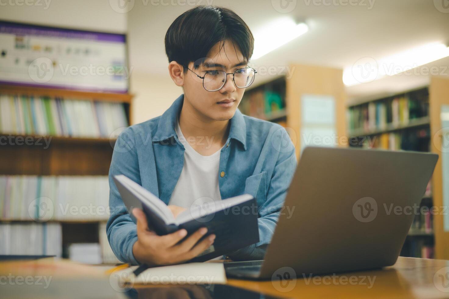 Male college students are working on laptops and searching for books to study, make reports, find useful information in college room. Concept of reading, learning and intelligence. photo