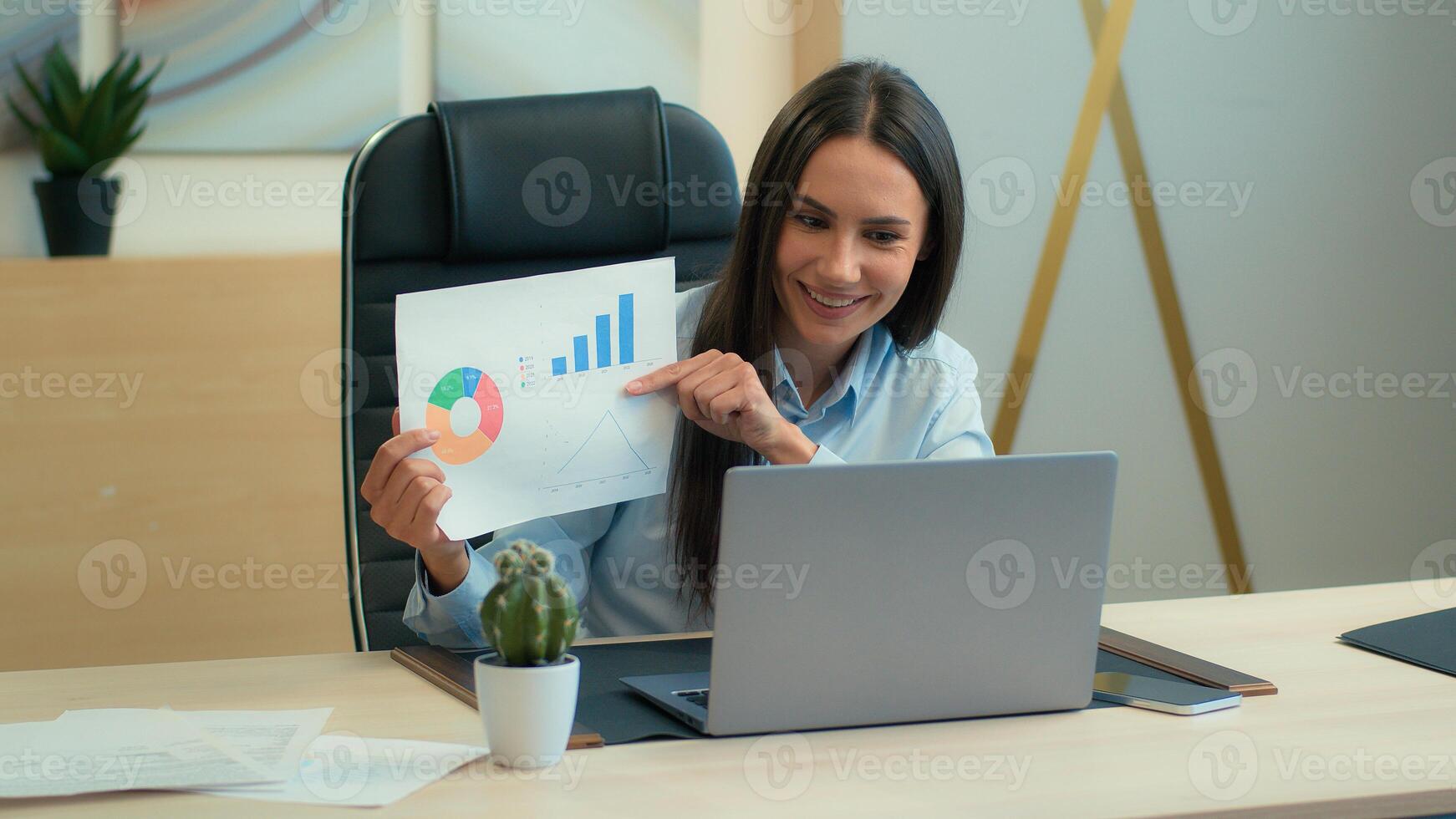 Cheerful happy Caucasian woman smiling business girl female businesswoman expert manager discuss talk call online on laptop in office showing papers diagram sales charts graphs data analyzing photo