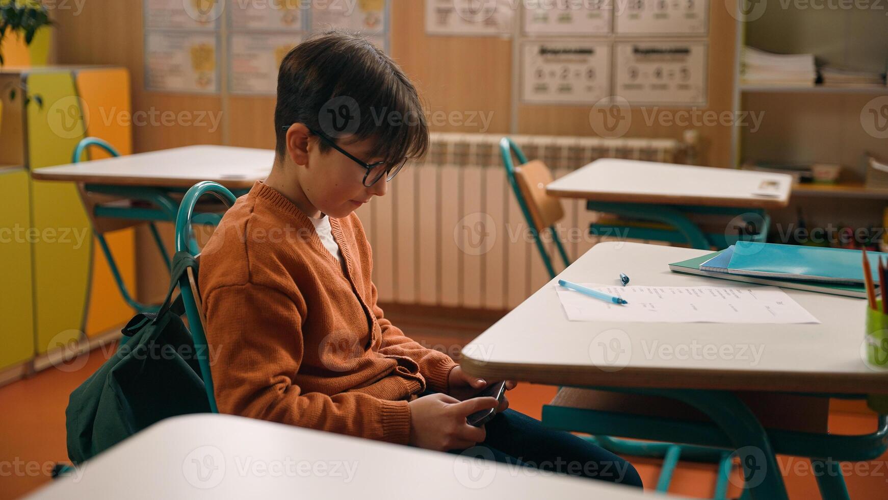 School education studying Caucasian boy little son schoolboy kid child pupil student schoolboy at class lesson gadget addict mobile phone addiction playing online game hide smartphone under desk photo